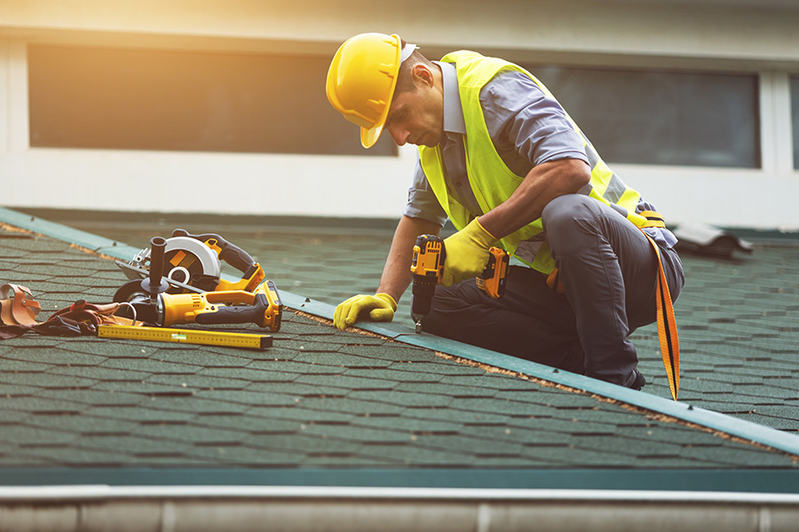 Specialized Business Insurance - A Contractor is on a Roof Using a Power Drill to Install a Roof Panel